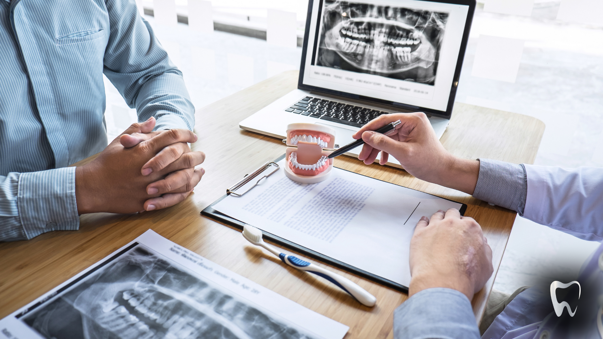 A dentist is talking to a patient at a table with a laptop.