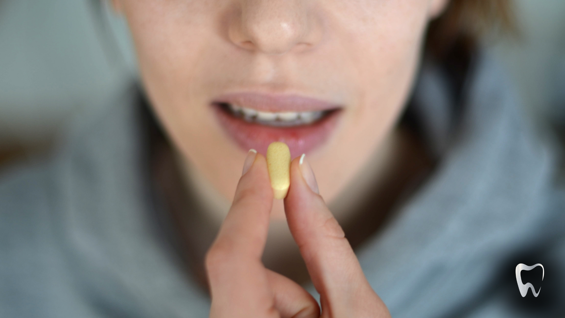 A woman is holding a pill in her hand in front of her mouth.