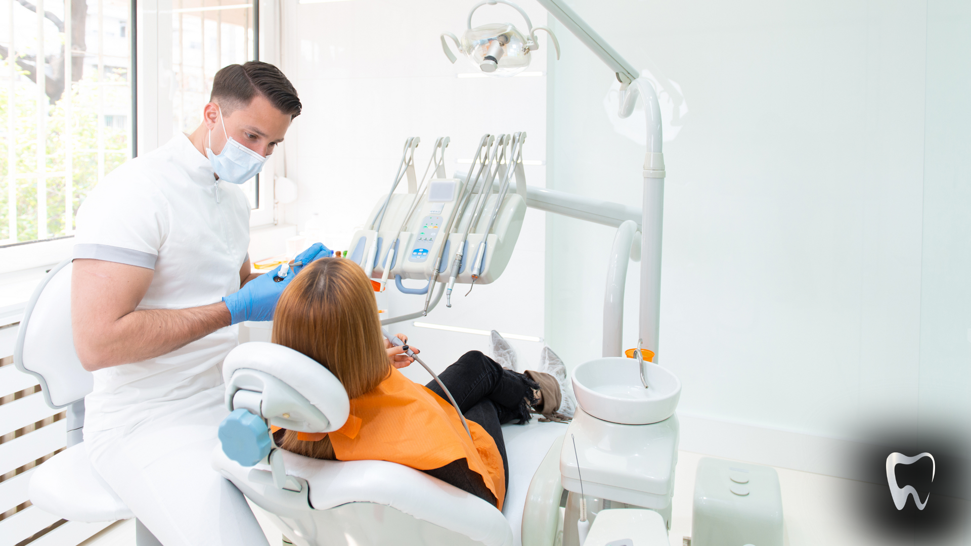 A woman is sitting in a dental chair while a dentist examines her teeth.