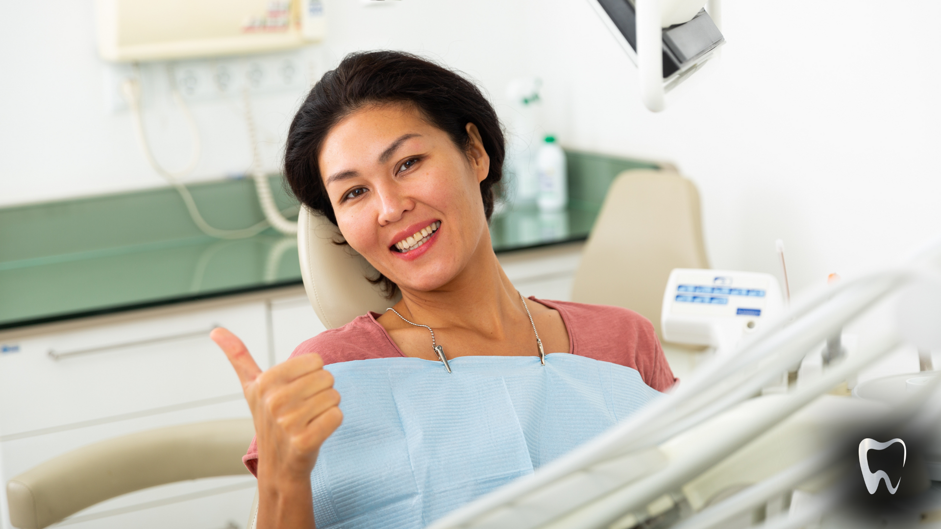 A woman is giving a thumbs up while sitting in a dental chair.