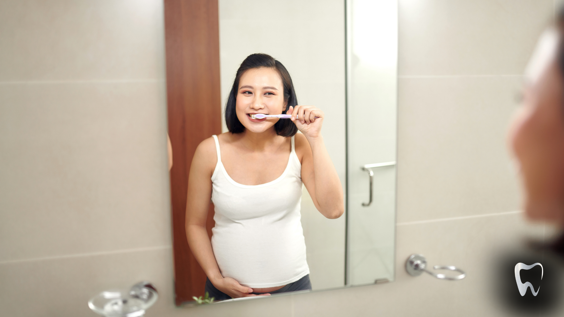 A pregnant woman is brushing her teeth in front of a bathroom mirror.