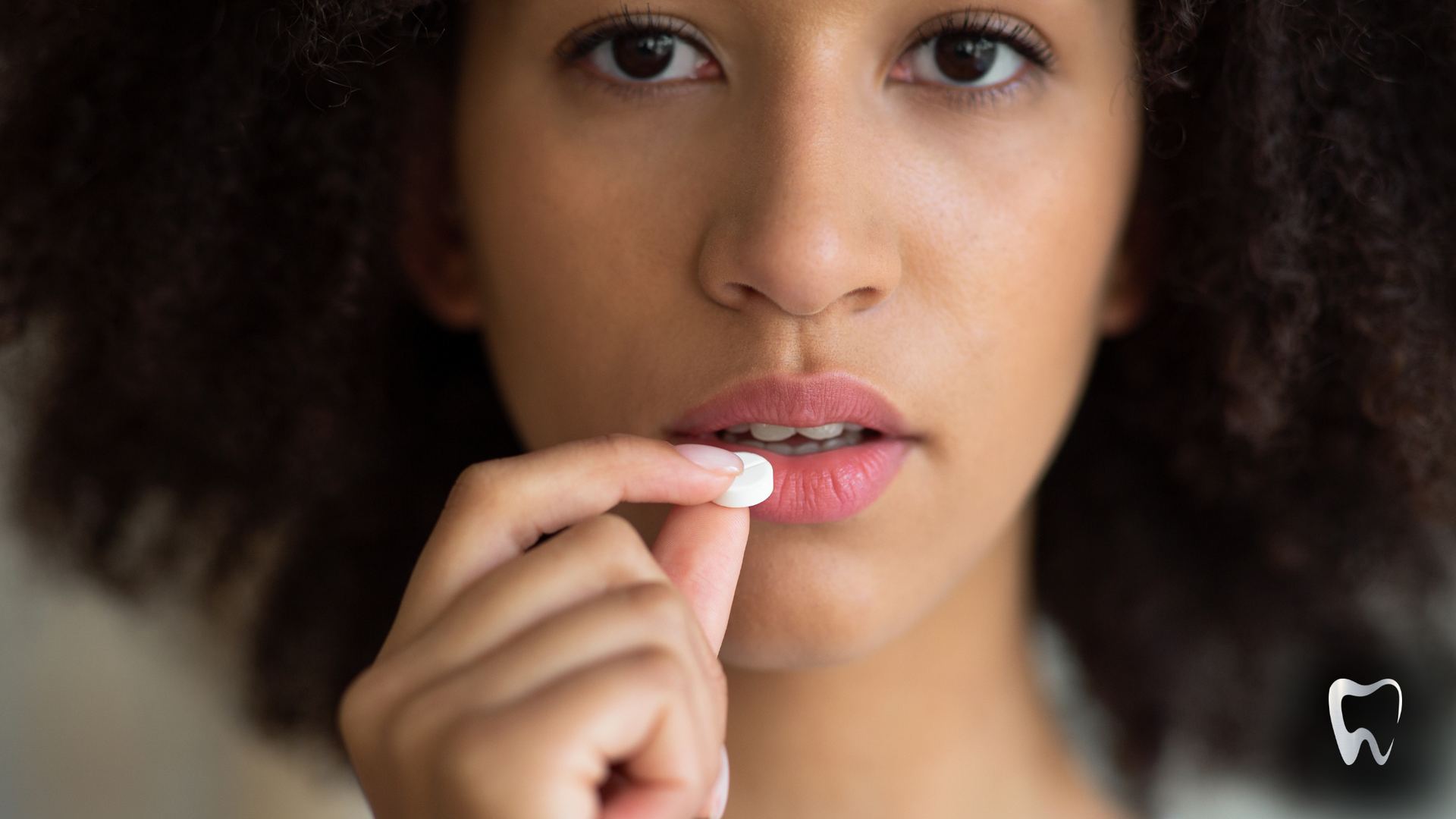 A woman is holding a pill in her hand in front of her mouth.