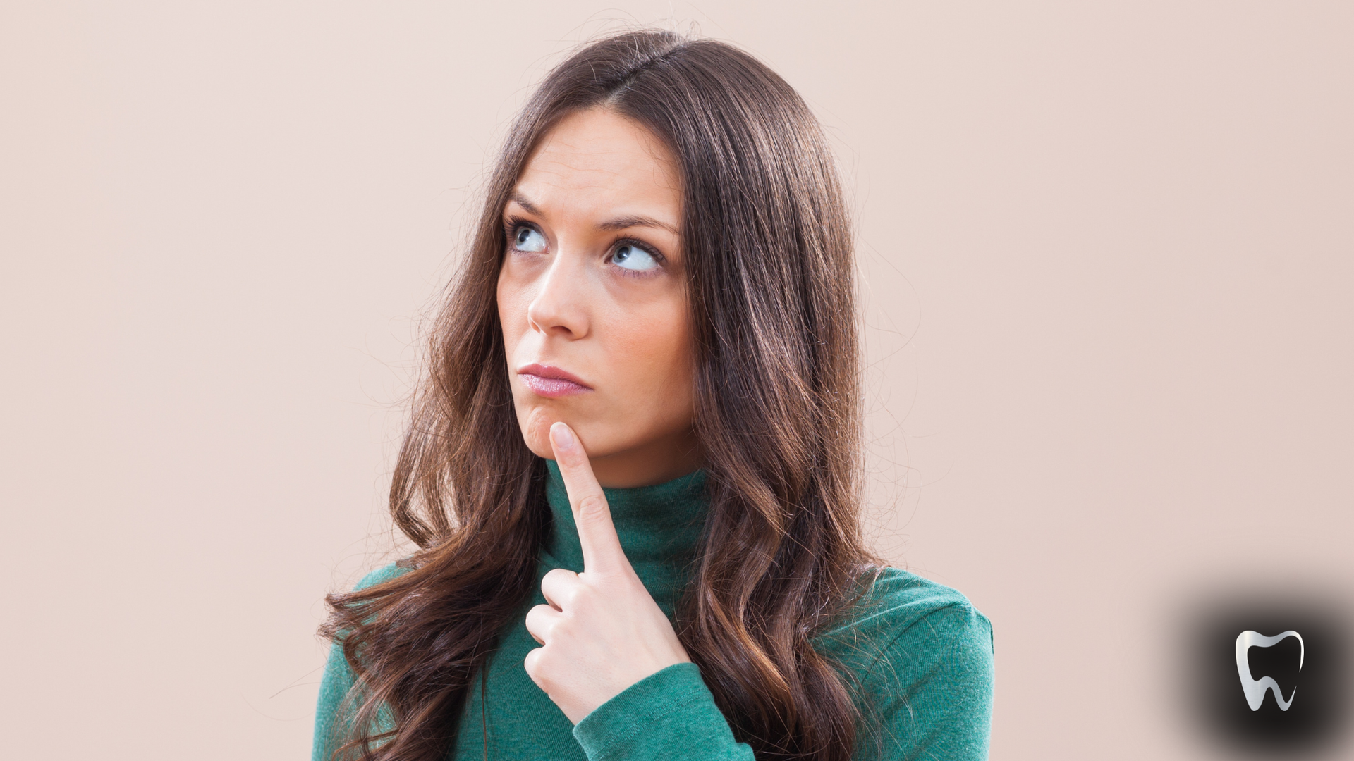 Woman in green turtleneck, looking up thoughtfully, finger on chin, against a neutral background.