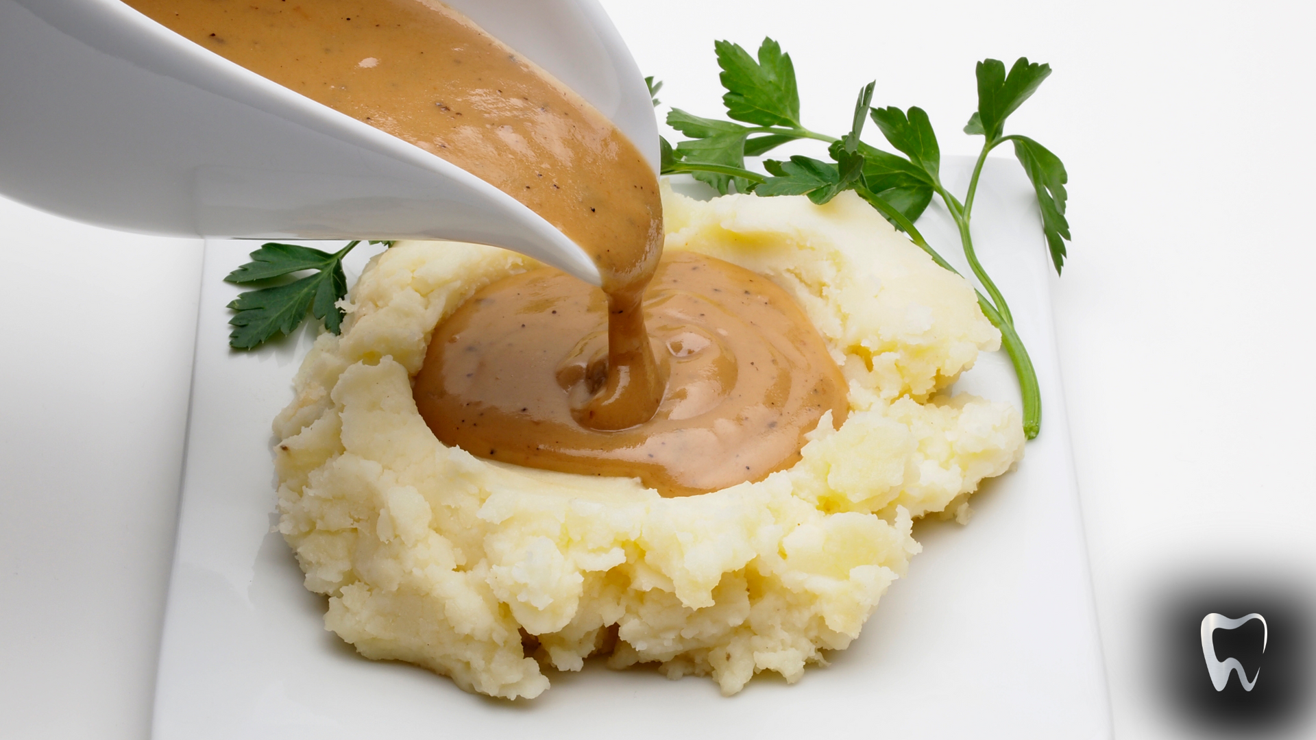 Gravy is being poured over mashed potatoes on a white plate