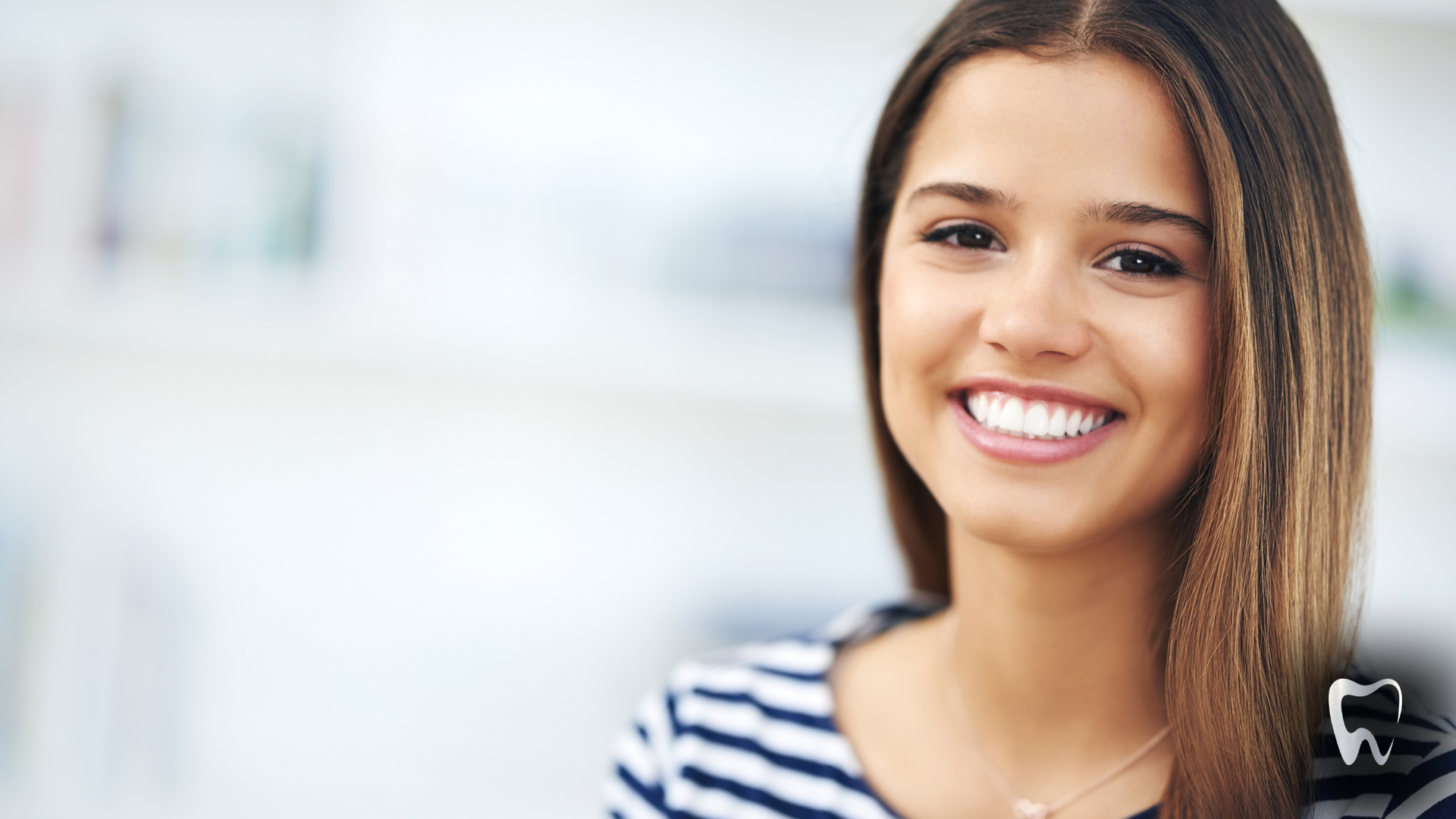 Woman with straight brown hair smiles, wearing a striped shirt in a bright room.