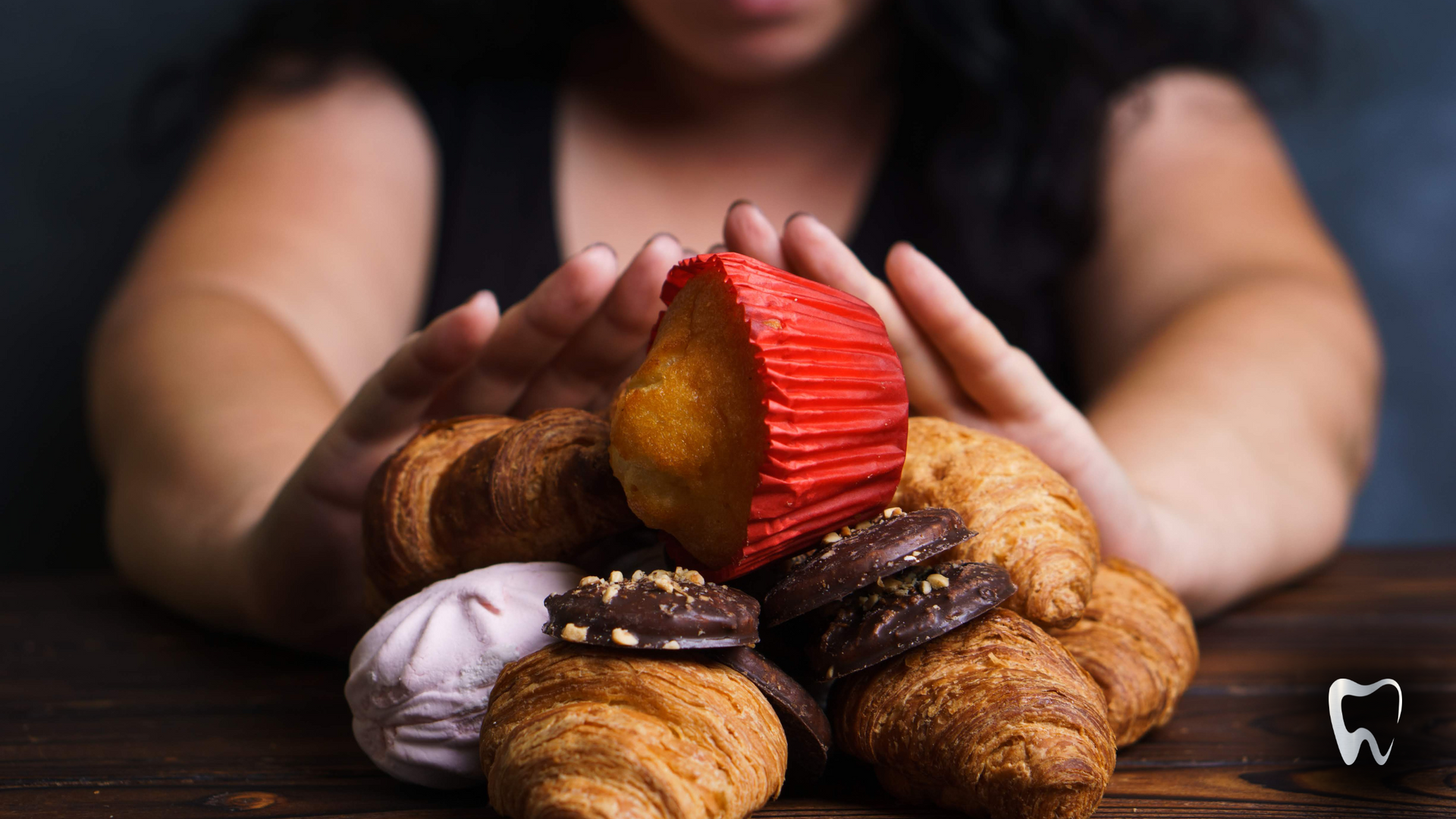 A woman is sitting at a table holding a pile of pastries.