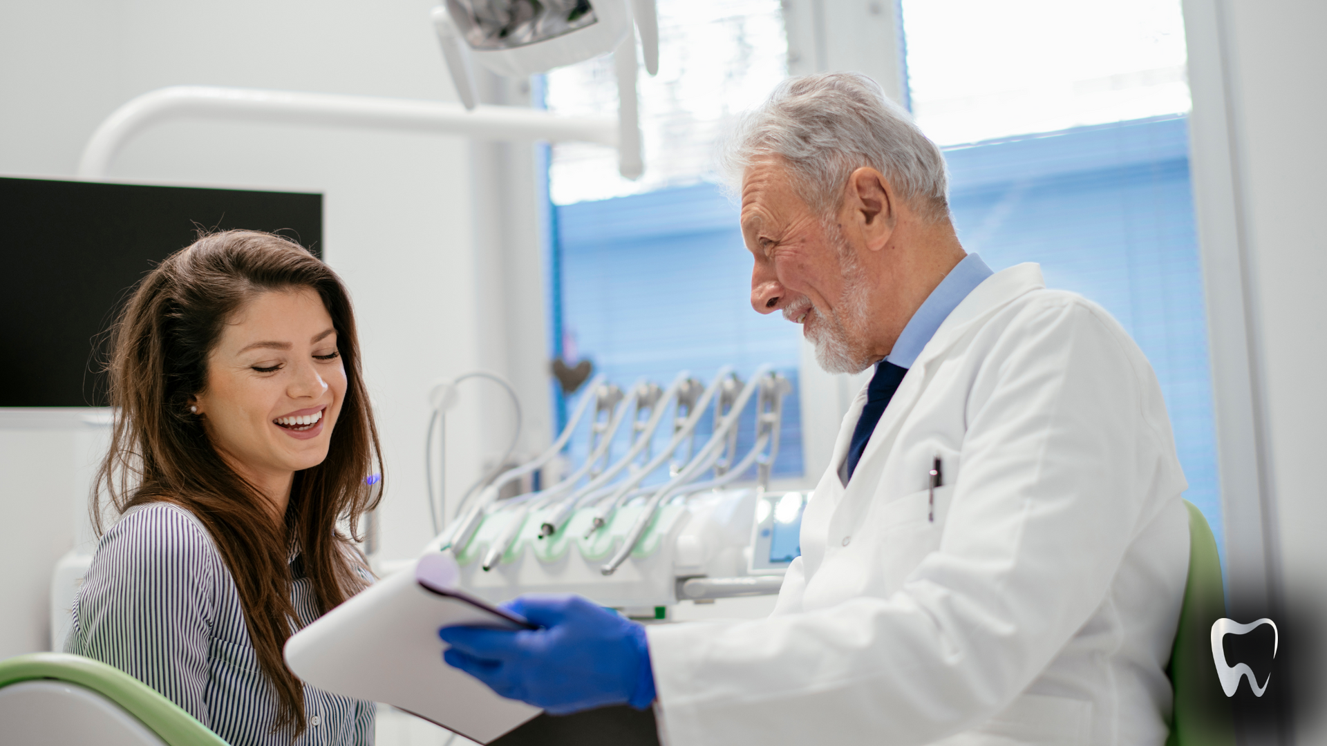 A dentist in a white coat reviews a document with a smiling female patient in a dental office.
