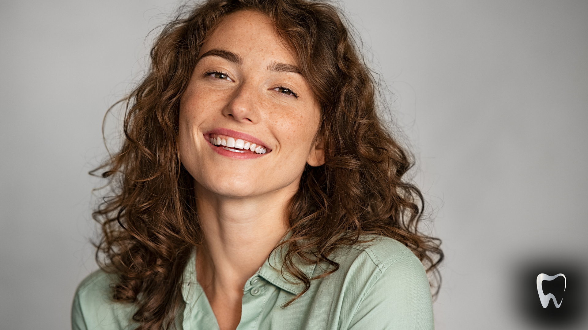 A woman with curly hair is smiling and wearing a green shirt.