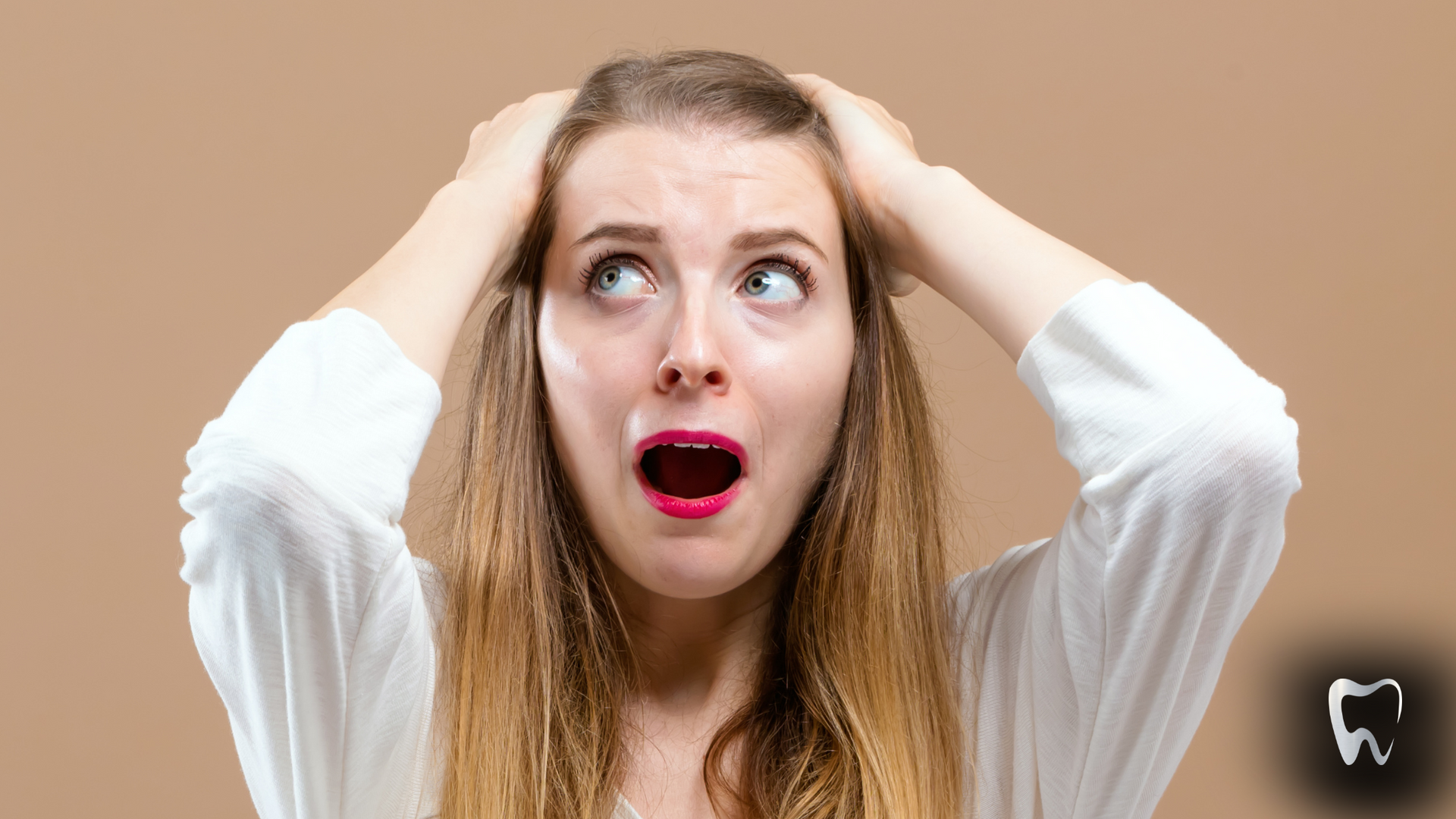 Woman with hands on head, mouth open in shock against beige background.