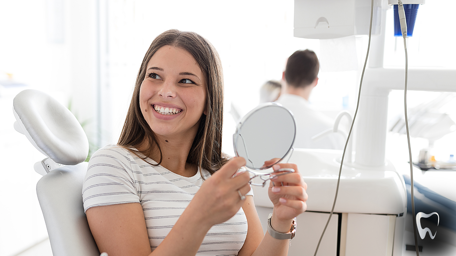 A woman is sitting in a dental chair looking at her teeth in a mirror.