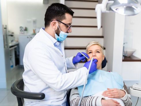 A dentist is examining a woman 's teeth in a dental office.