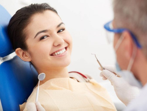 A woman is smiling while sitting in a dental chair while a dentist examines her teeth.