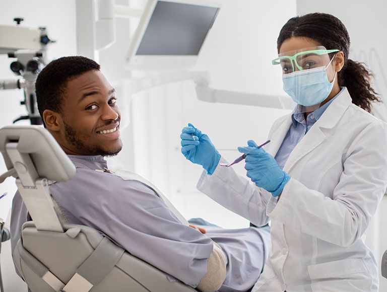 A man is sitting in a dental chair while a female dentist examines his teeth.