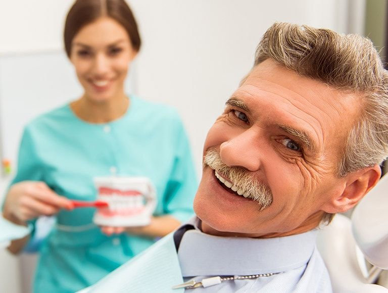 A man is sitting in a dental chair while a woman holds a model of teeth.