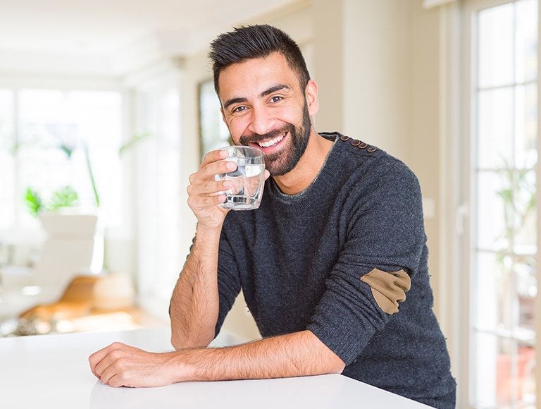 A man is sitting at a table drinking a glass of water.