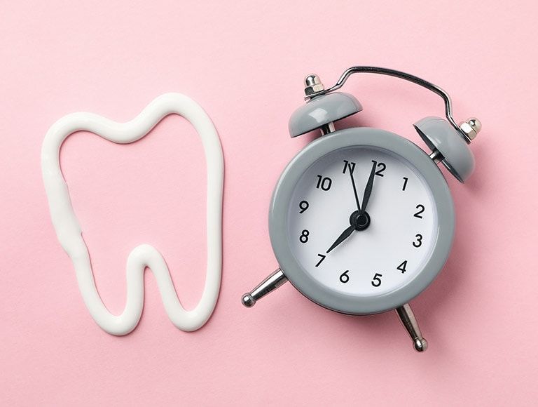 A tooth made of toothpaste next to an alarm clock on a pink background.