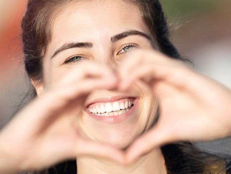 A woman is smiling and making a heart shape with her hands.