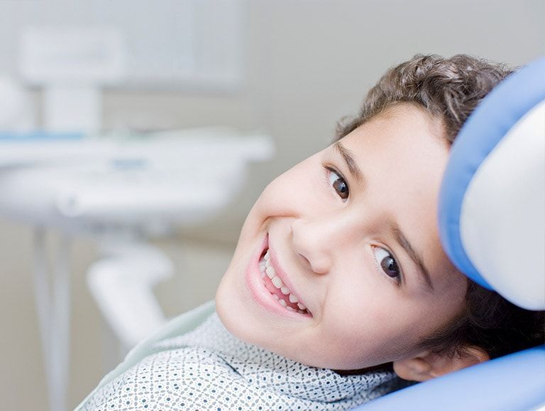 A young boy is smiling while sitting in a dental chair.