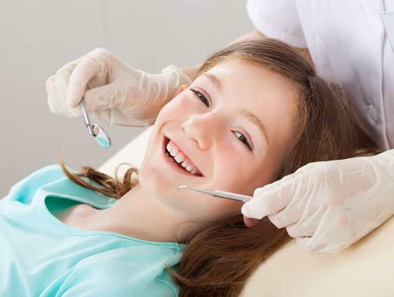 A little girl is getting her teeth examined by a dentist.