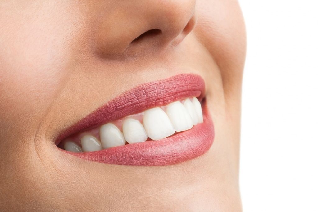 A close up of a woman 's smile with white teeth and red lipstick.