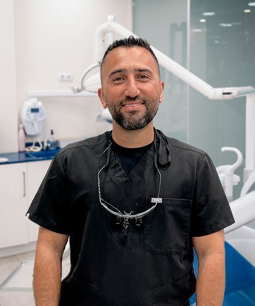 A man wearing a black scrub and glasses is standing in front of a dental chair