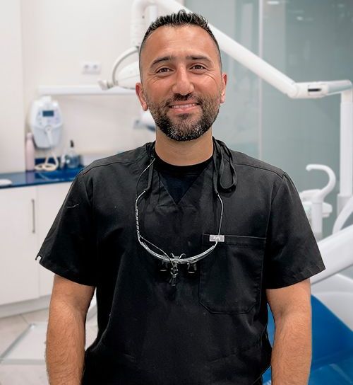 A man wearing a black scrub and glasses is standing in front of a dental chair