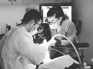 A dentist and a nurse are working on a patient 's teeth in a black and white photo.