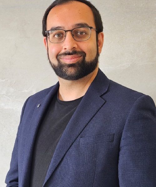 A man with a beard wearing glasses and a blue jacket