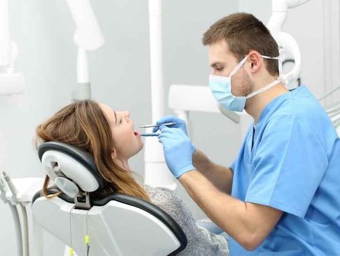 A woman is sitting in a dental chair while a dentist examines her teeth.