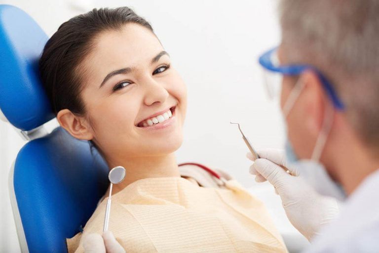 A woman is sitting in a dental chair while a dentist examines her teeth.