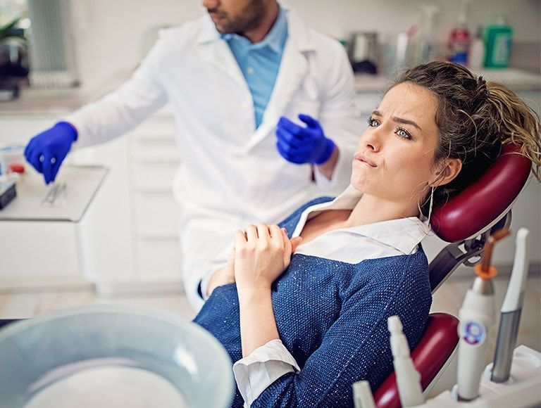 A woman is sitting in a dental chair while a dentist examines her teeth.