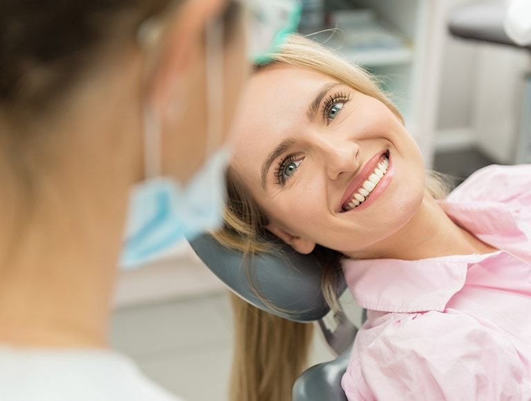 A woman is smiling while sitting in a dental chair.