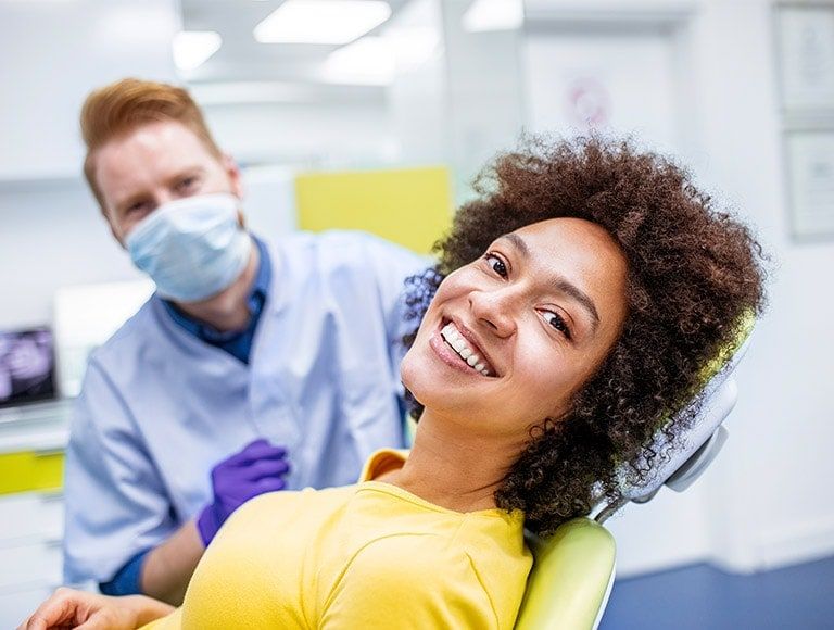 A woman is smiling while sitting in a dental chair.