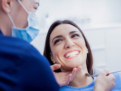 A woman is smiling while having her teeth examined by a dentist.