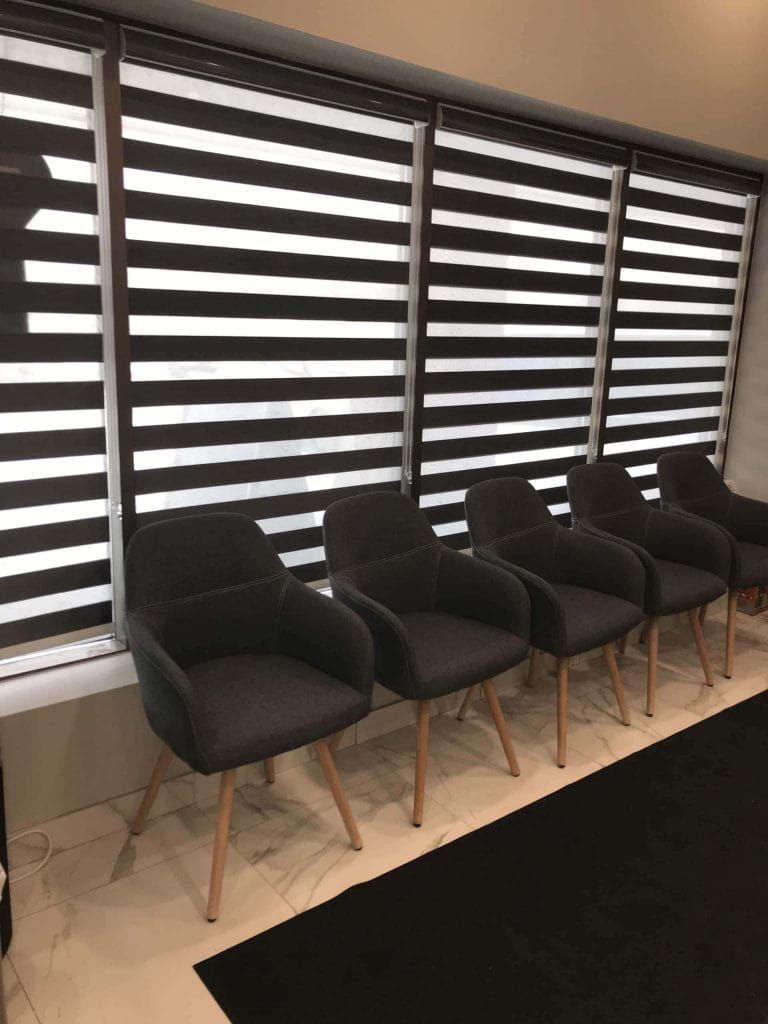 A row of chairs in a waiting room with blinds on the windows.
