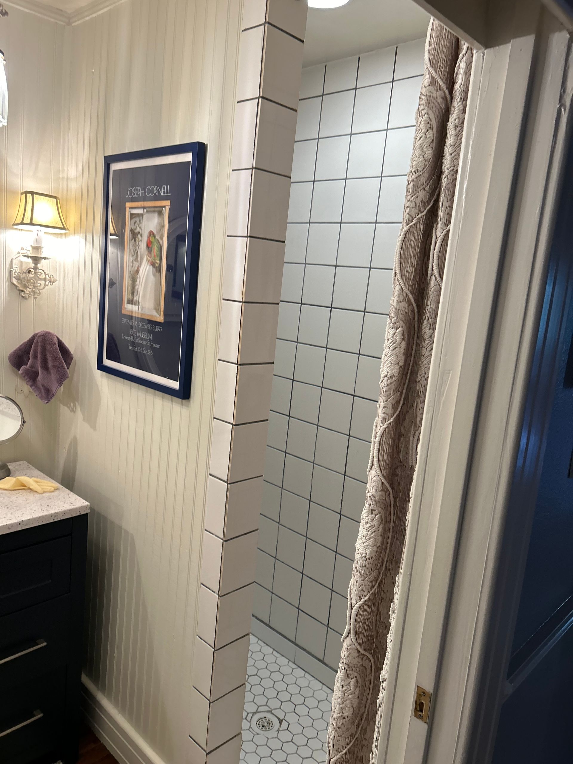 Bathroom with shower. White-tiled shower, partially open, next to a sink area with blue cabinet.