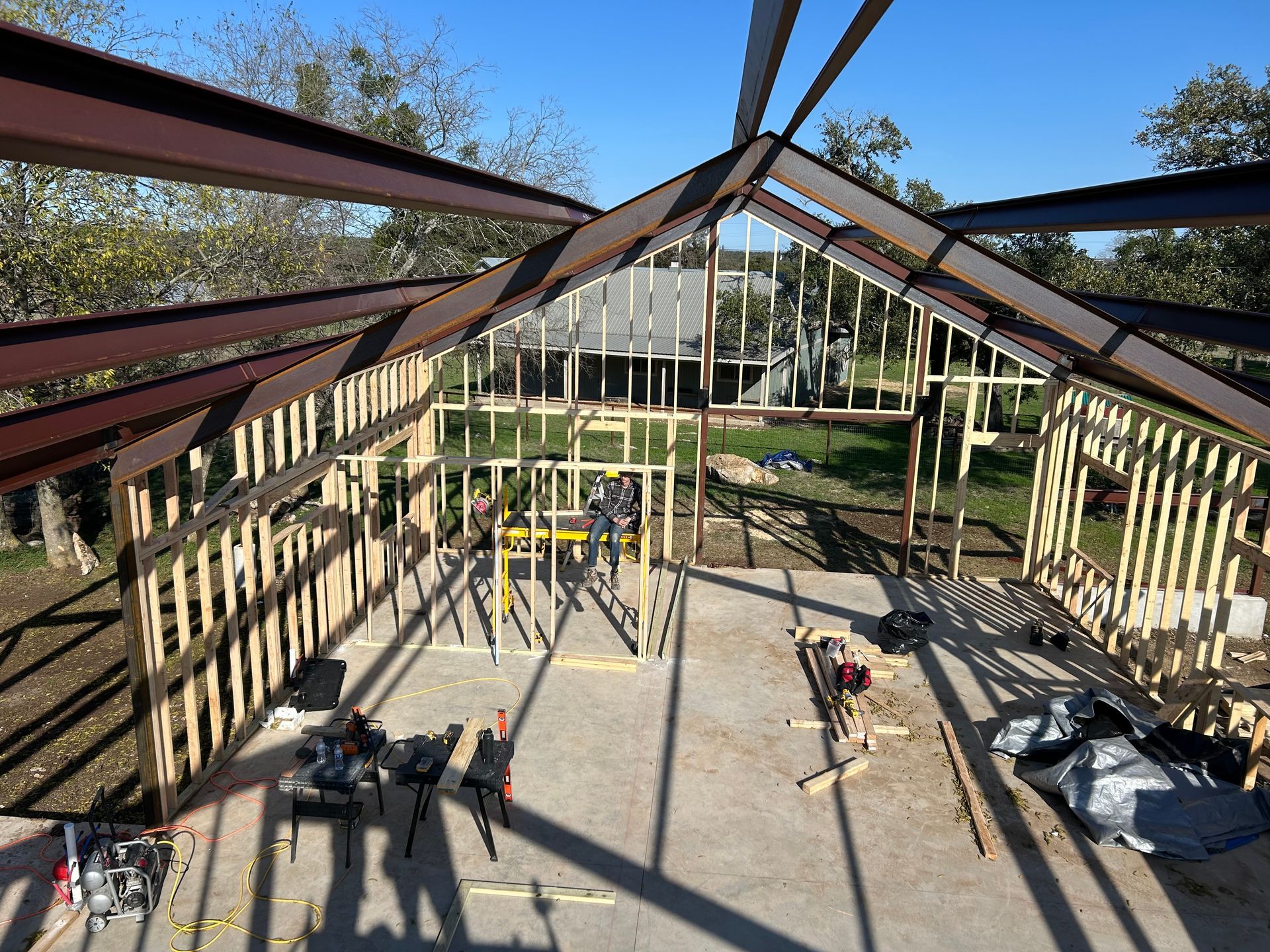 Construction site: Steel beams frame wood-framed walls on a concrete slab, under a blue sky.