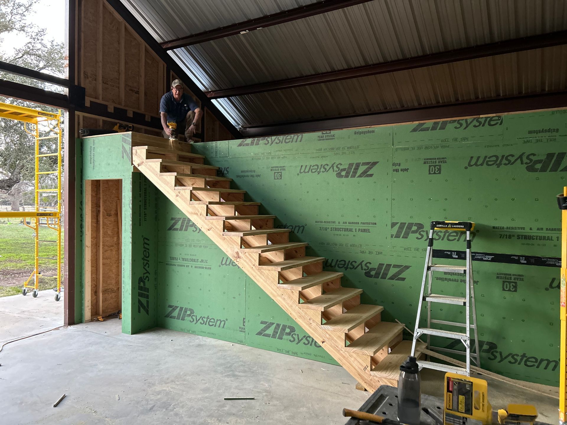 Man building wooden stairs inside a metal-framed structure, using a level.