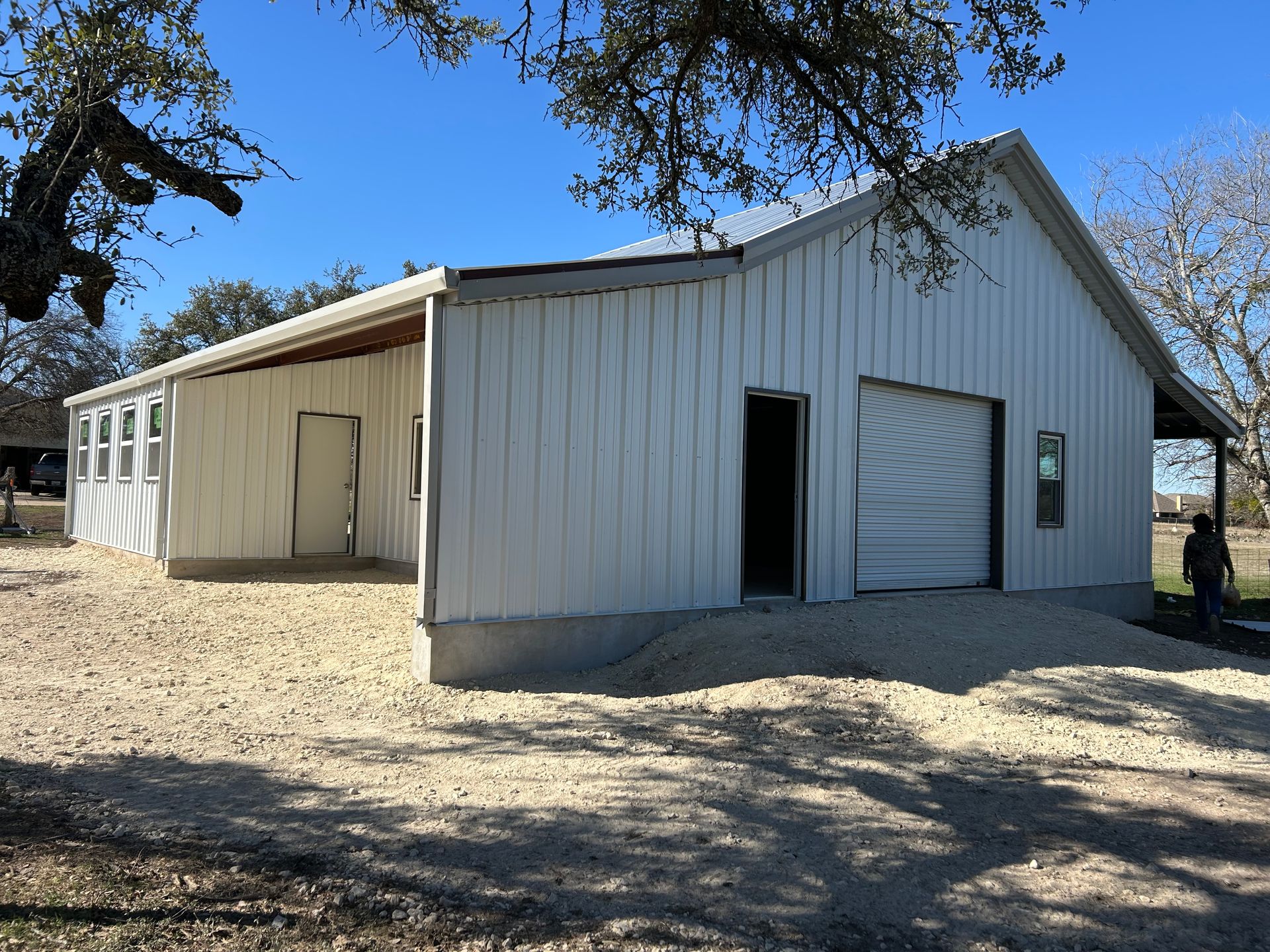 White metal building with open garage door, windows, and gravel driveway.