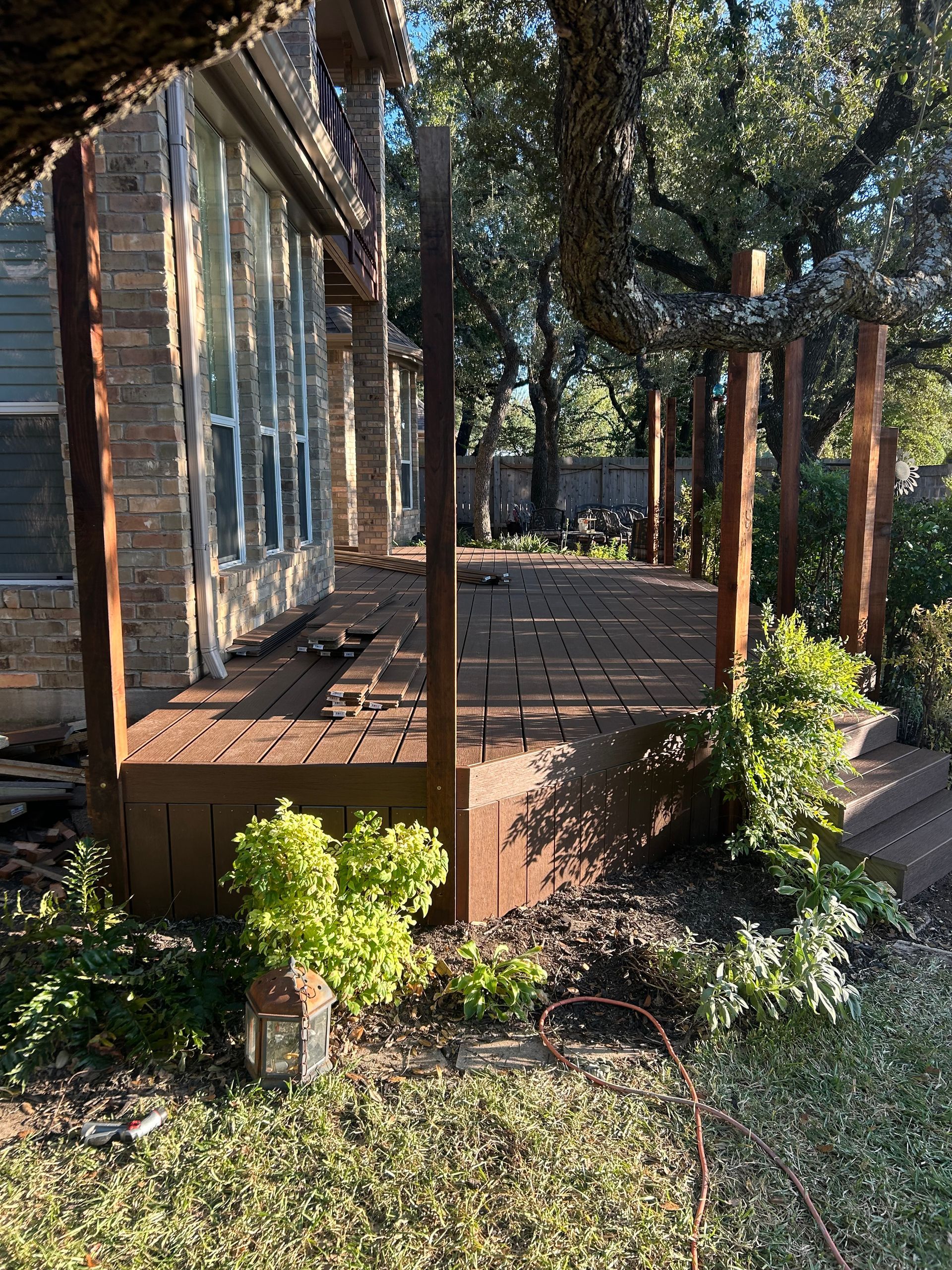 Wooden deck with posts, plants, and a house.