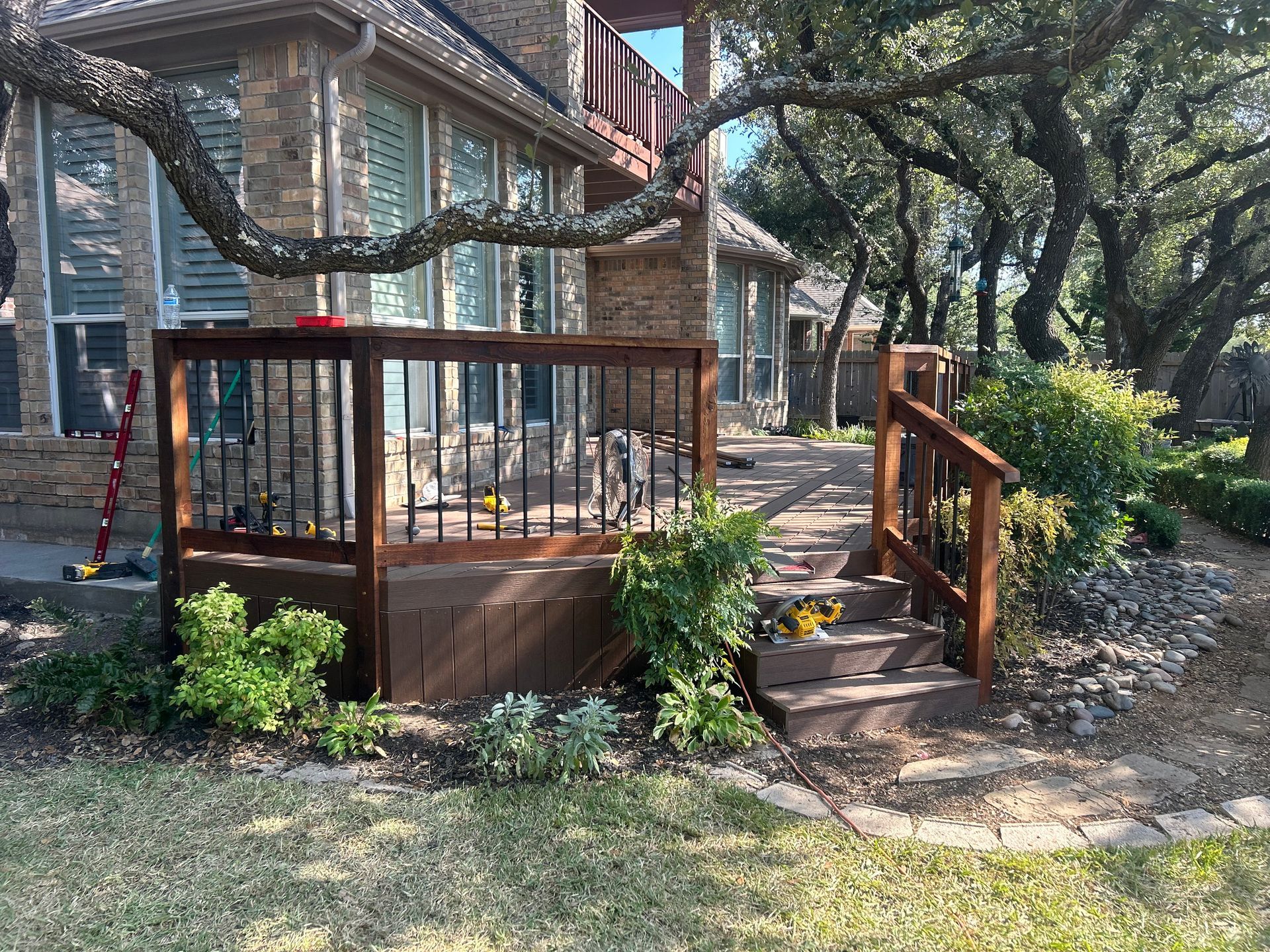 Wooden deck with railing, steps, and landscaping next to a brick house.