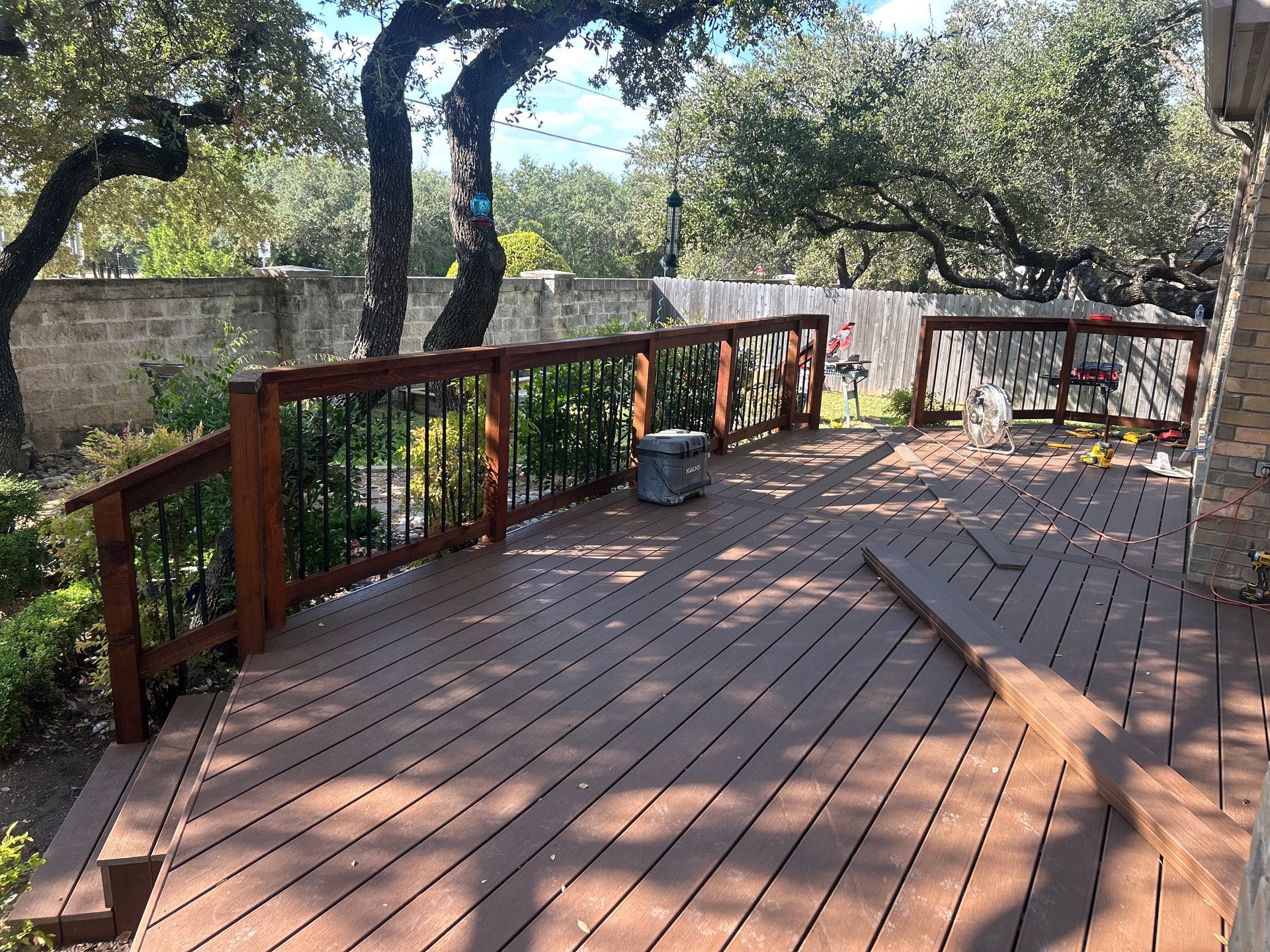 Wooden deck with railing, surrounded by trees and a stone wall.