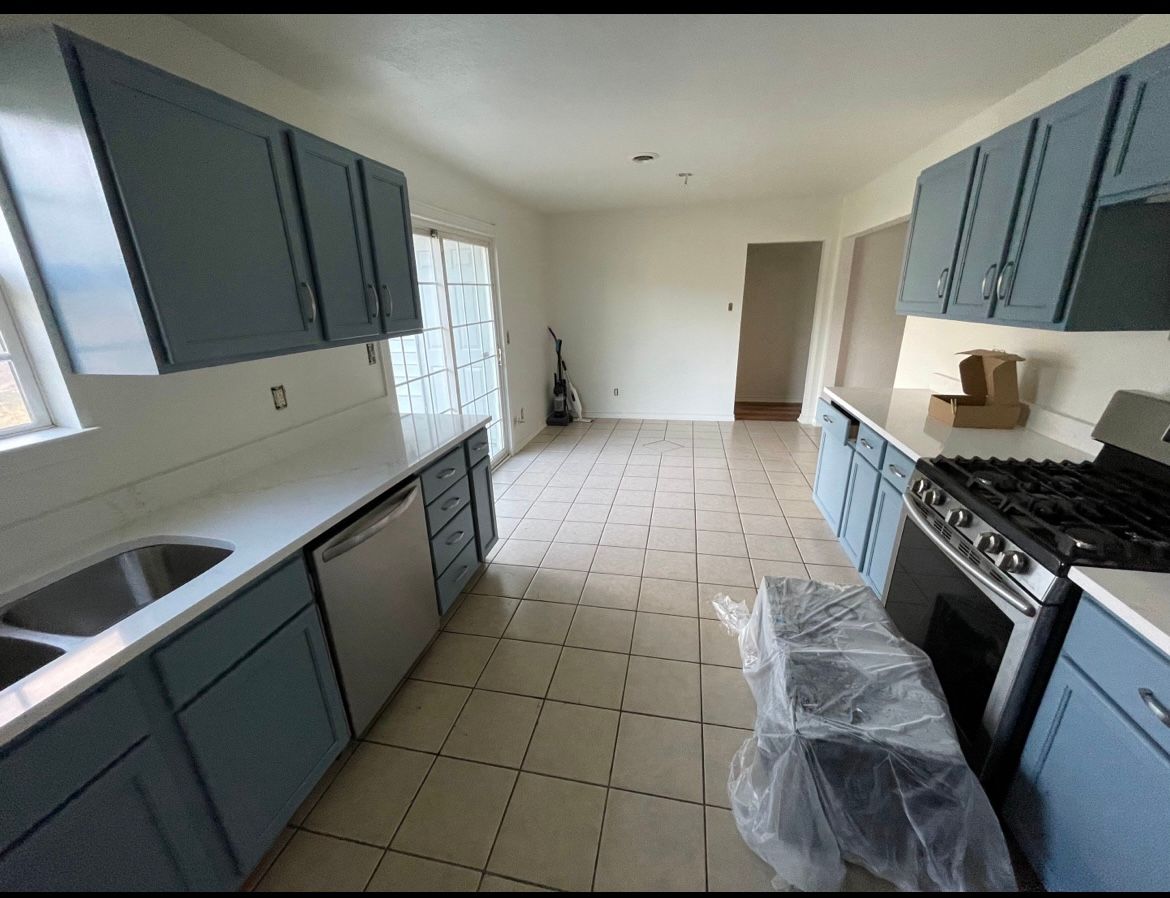 Kitchen with blue cabinets, white countertops, stainless steel appliances, and tile flooring.