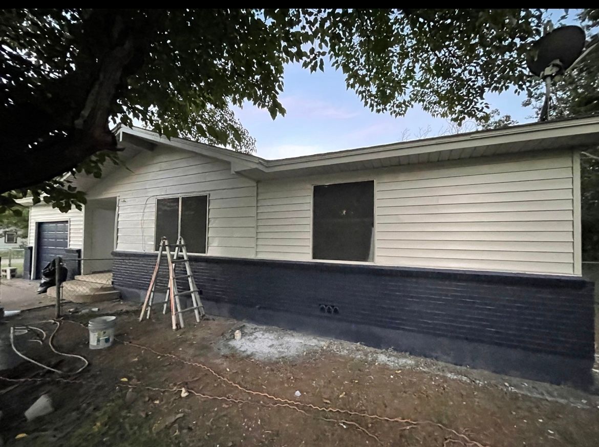 House with white siding and dark blue brick, construction materials nearby.
