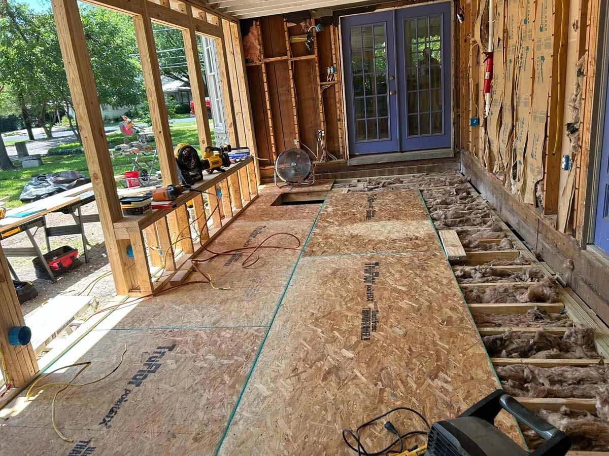 Sunroom under construction; exposed framing, OSB flooring, blue door in background.