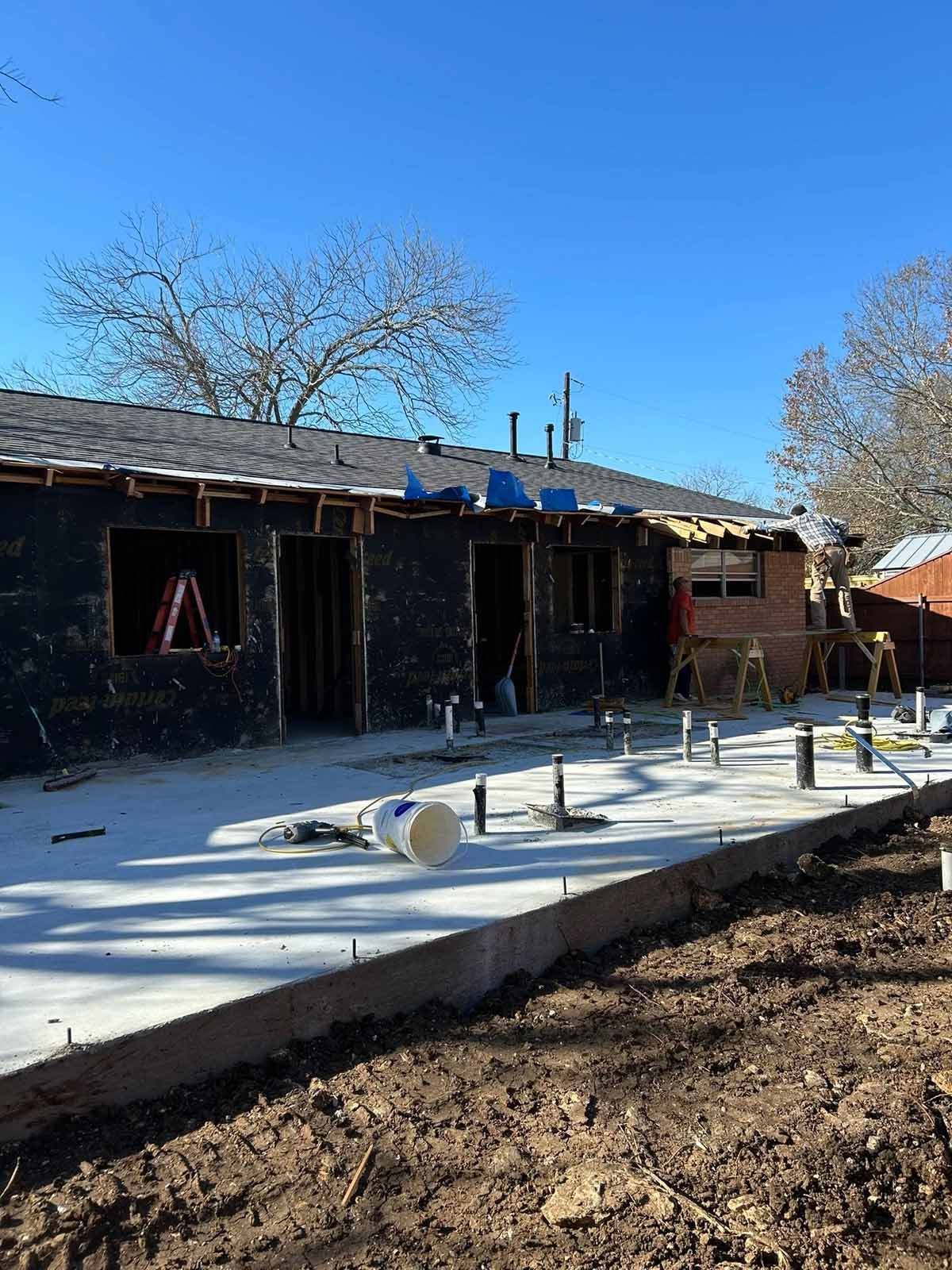 Construction site; concrete slab, unfinished building with exposed framing, blue sky.