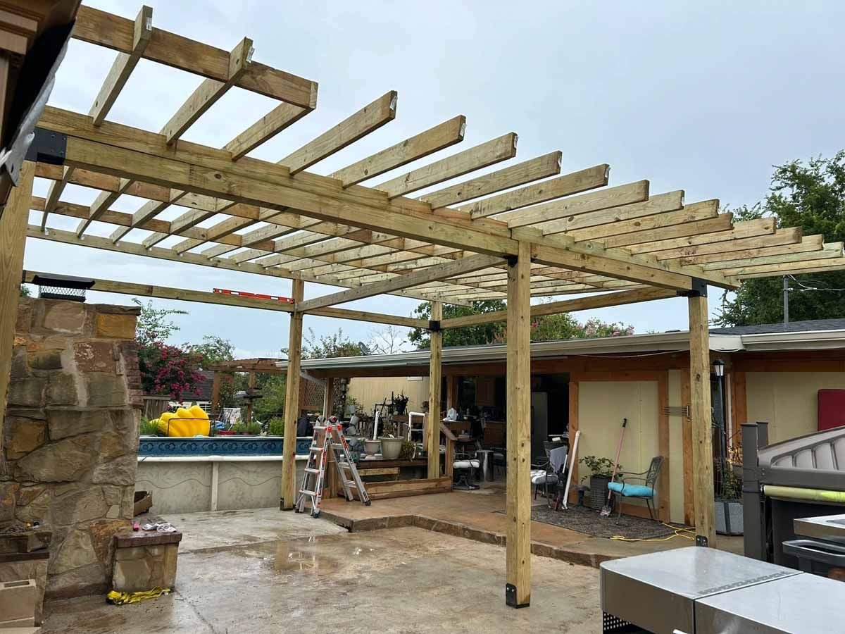 Wooden pergola under construction in a backyard, with a pool and a house visible in the background.