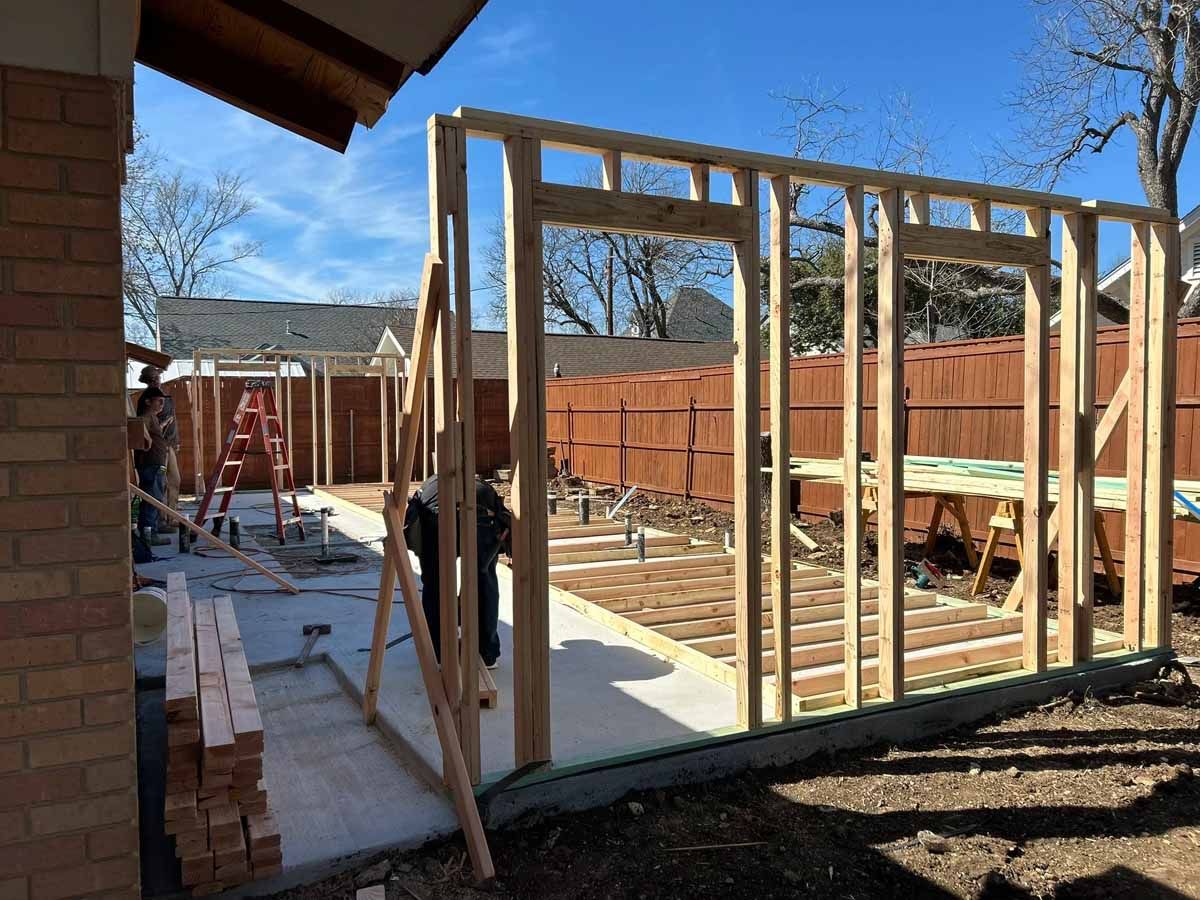 Wooden framework of a building under construction outdoors. A few people work. Sunny day.