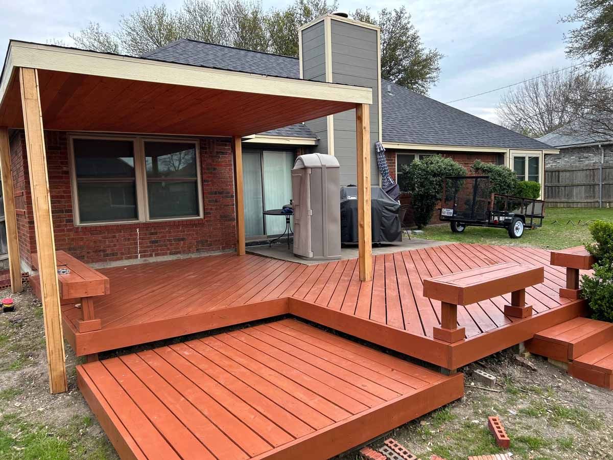 Red-painted wooden deck attached to a brick house, featuring a covered area and built-in bench.
