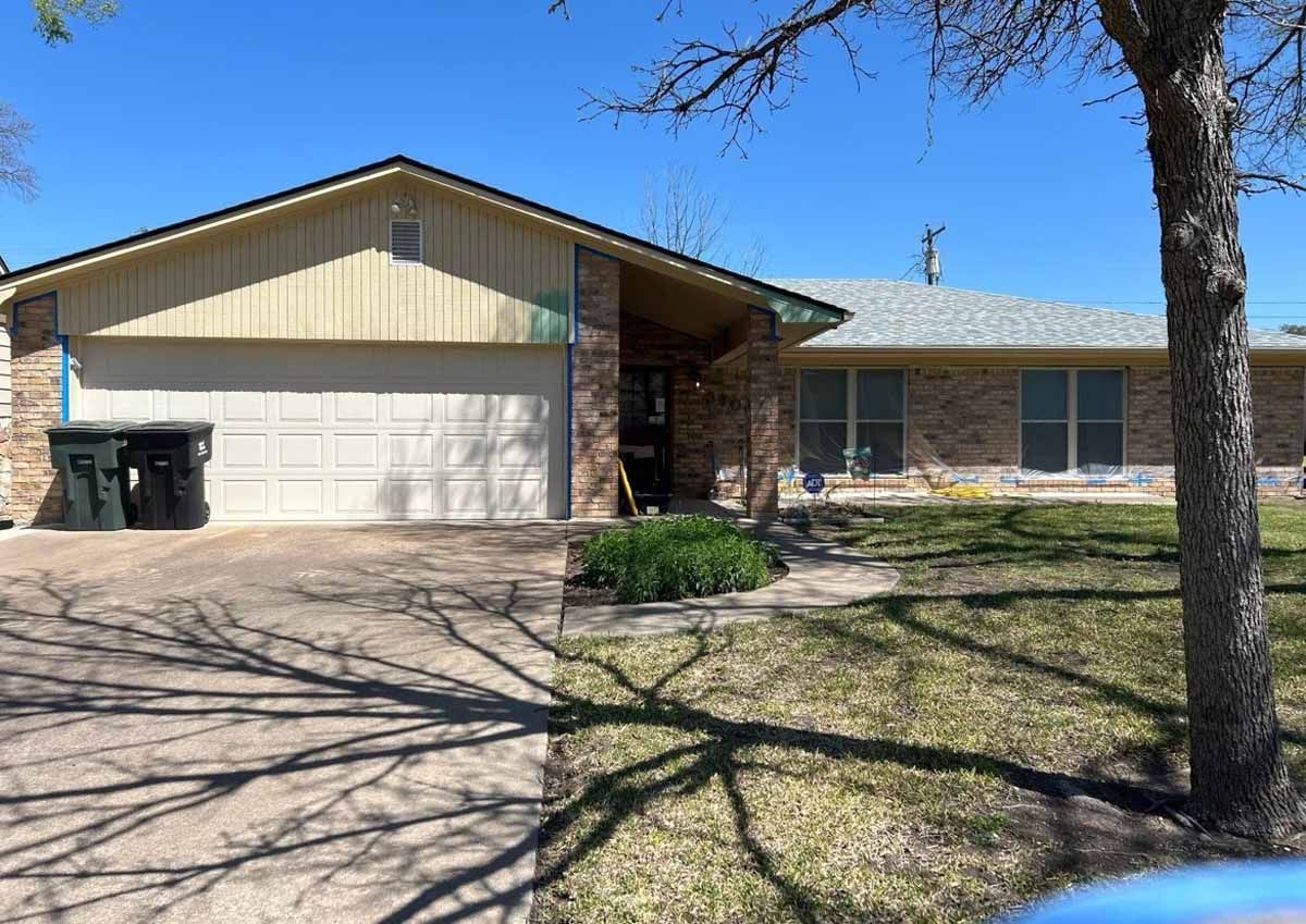 Tan brick home with attached garage, driveway, and front lawn under a bright blue sky.